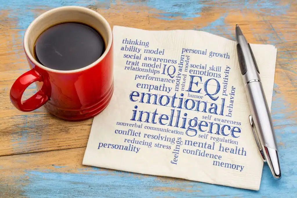 emotional intelligence and other words that describe it written on a brown napkin with a red cup of black coffee beside it