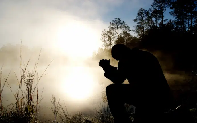 Silhouette of a person praying outdoors at sunrise, representing faith, reflection, and the spiritual focus of Christian counseling.