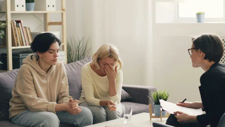 Teen and parent sitting together during a family therapy session with a counselor at Redeemed Life Counseling, discussing emotional challenges in a safe and supportive environment