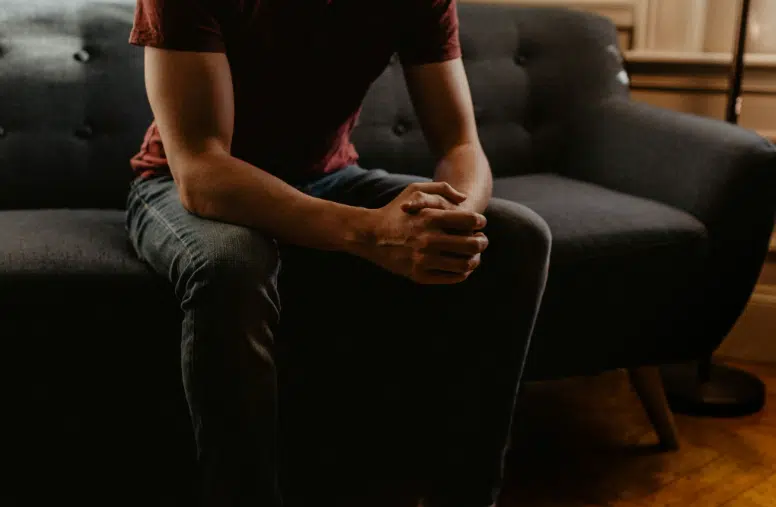 Person sitting with hands clasped in a dimly lit room, reflecting emotional stress and anxiety before or during a counseling session