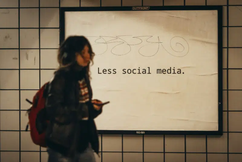 Teen walking past a sign that says “Less social media,” representing the impact of social media on teen anxiety and emotional health.