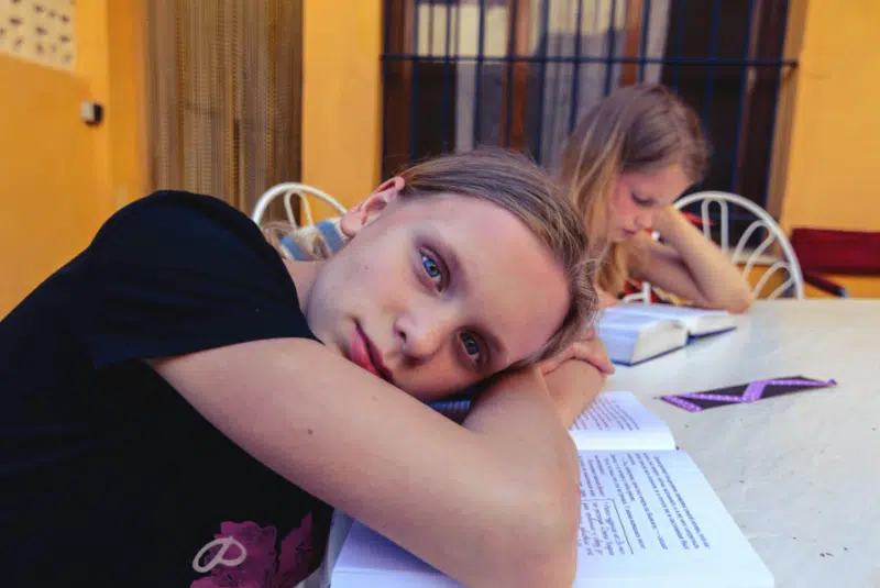 Teen girl resting her head on a table while studying, representing emotional overwhelm, stress, and adolescent anxiety.