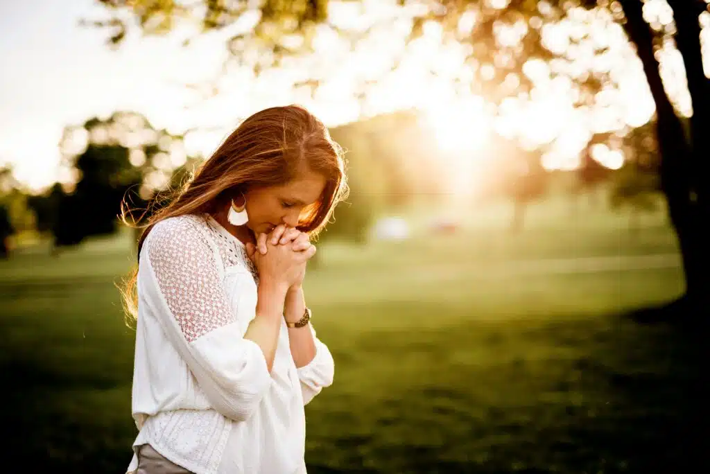 Woman praying outdoors in golden sunlight with hands clasped representing faith, hope, and healing through Christian trauma counseling