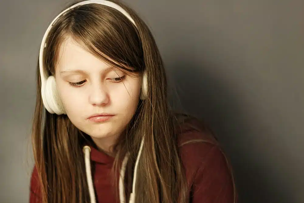 Sad teenage girl wearing headphones and looking down, representing emotional withdrawal and possible signs of depression in adolescents.