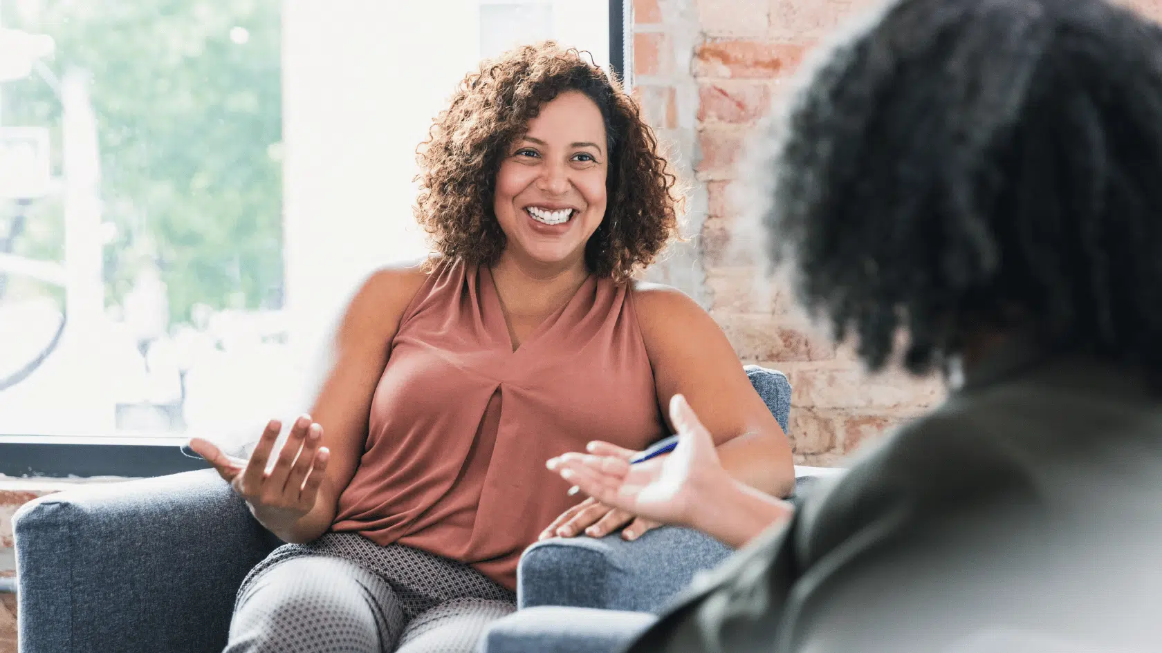 TWoman sitting comfortably in an armchair and smiling as she talks with her therapist in a bright, welcoming counseling office.