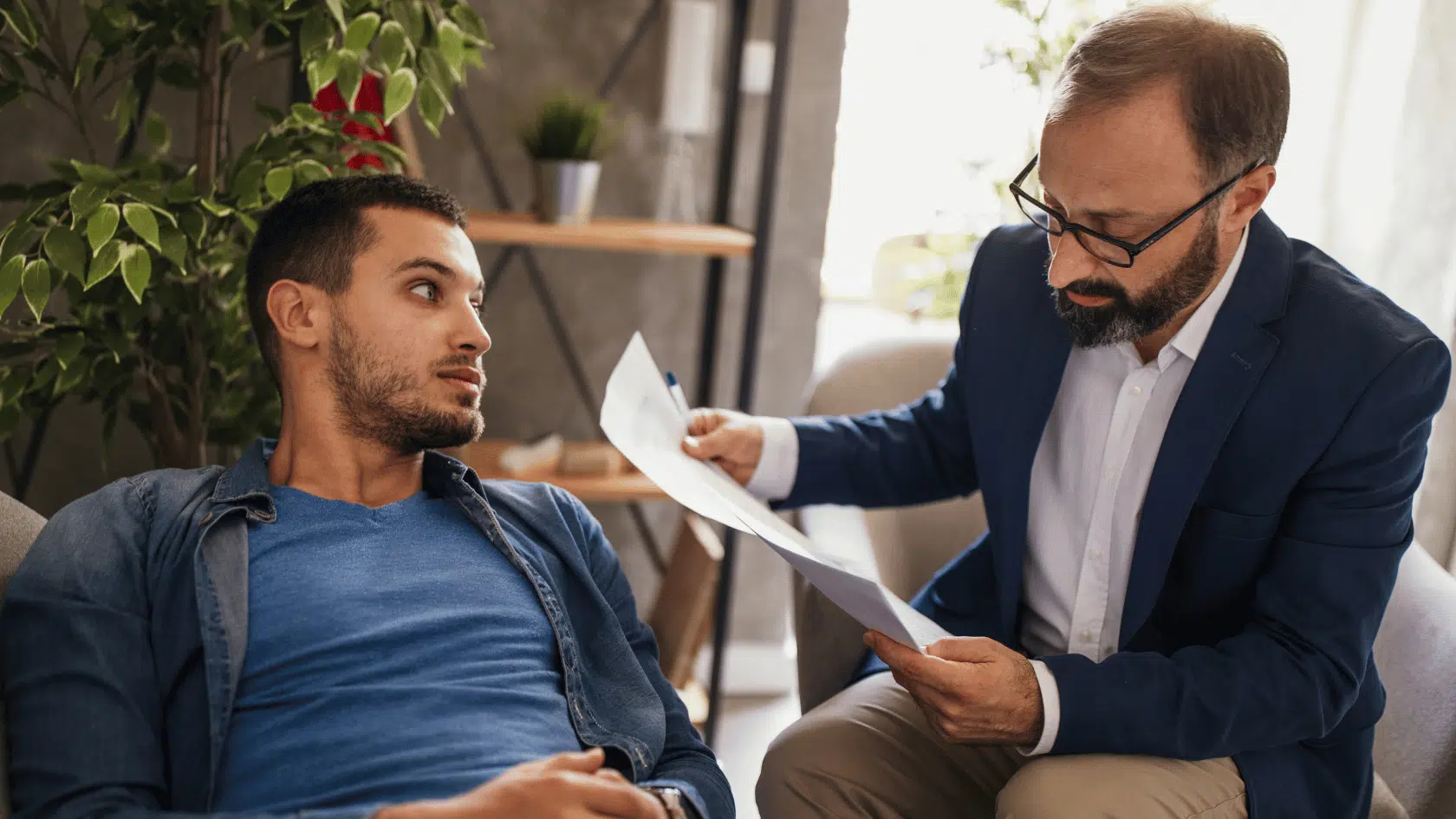 Therapist holding notes and speaking with a seated client in a calm office, guiding him through a brain based therapy session.